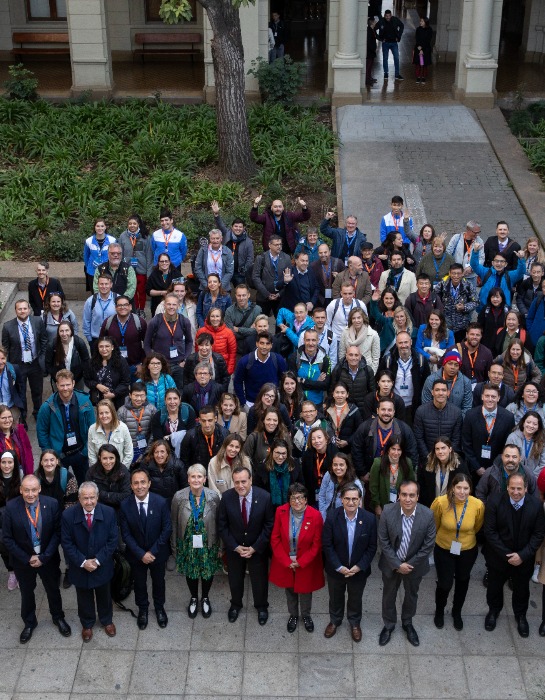 Imagen muestra a varios participantes de la conferencia AIESEP 2023 saludando a la cámara al interior del campus Casa Central de la PUC.