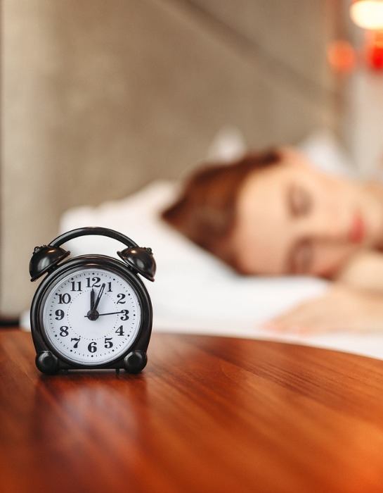 Mujer duerme mientras imagen capta primer plano de reloj despertador.