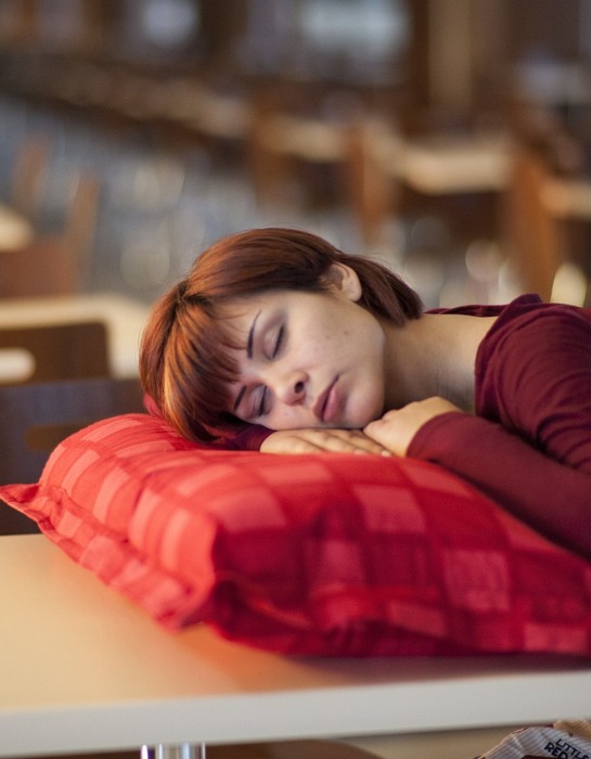 Imagen muestra a mujer durmiendo al interior de una biblioteca.